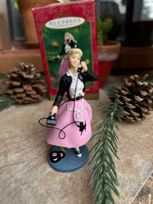 Decorative Barbie ornament figurine with a pink and black 50's theme outfit on a surface with an old fashioned telephone 