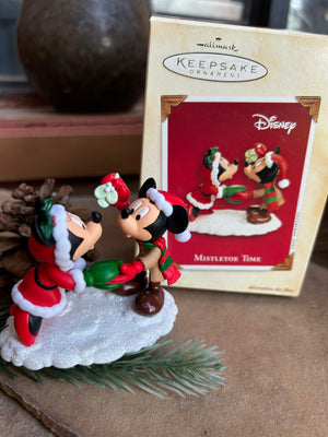 A Hallmark Keepsake ornament featuring Mickey and Minnie Mouse under the mistletoe, with the ornament box in the background.