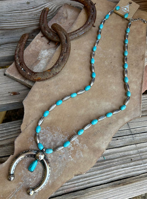 Necklace with turquoise beads and silver horseshoe charm on a rustic wooden surface