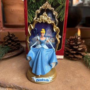Disney Cinderella figurine in a blue dress with gold accents, displayed against a textured wall.