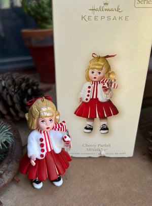 Christmas ornament of a girl in a red dress with a box labeled 'Hallmark Keepsake'.