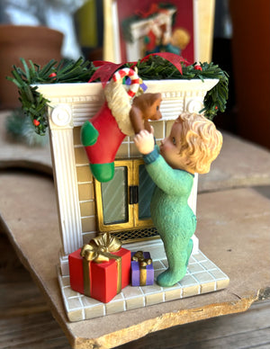 Decorative keepsake ornament  of a child reaching into a stocking by a fireplace with presents and a beautiful message on the back of the fireplace 