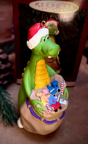 Decorative Dudley the Dragon a Keepsake Christmas ornament of a green dragon with a Santa hat, standing ready to hand out a bag of Christmas Gifts  