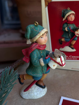 Christmas Nostalgic Keepsake  ornament of a young boy in his green warm coat and bright red scarf playing with this hobby horse and getting ready for the holidays!