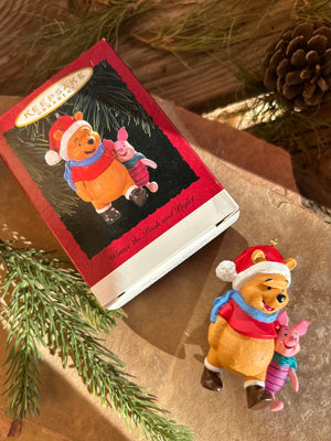A porcelain keepsake for hallmark ornament featuring Winnie the Pooh and Piglet in holiday outfits, presented next to its packaging.